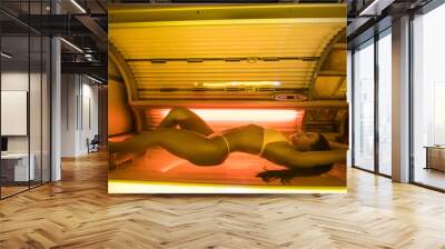 Young girl in a bathing suit sunbathing in a solarium, wants a beautiful tanned skin Wall mural